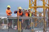 A group of men wearing high-vis clothing and hard hats stand on a worksite.