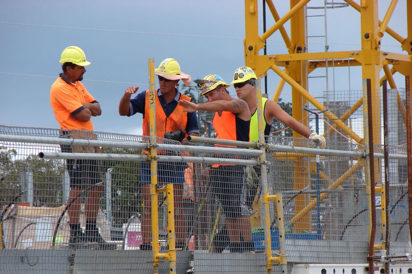 A group of men wearing high-vis clothing and hard hats stand on a worksite.