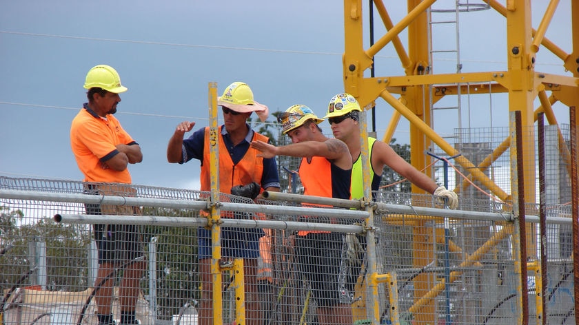 A group of men wearing high-vis clothing and hard hats stand on a worksite.