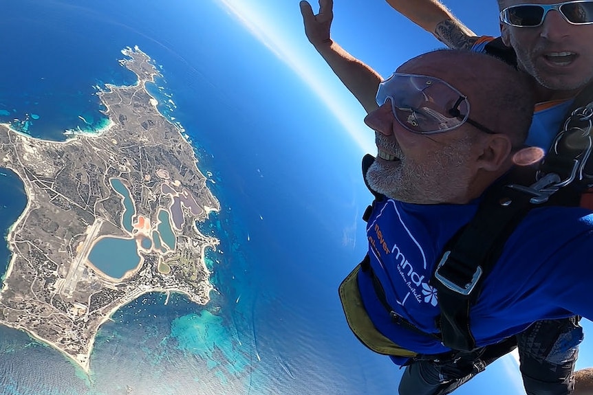 Two men skydiving over the ocean with an island underneath them.