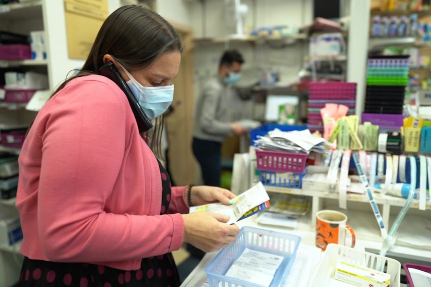 Pharmacist holding a prescription and speaking to a customer on the phone.