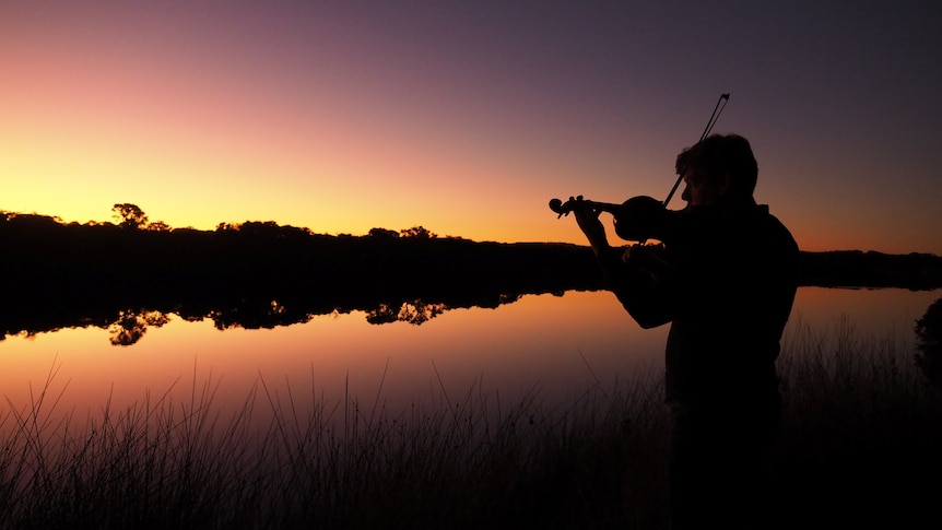 Silhouette of a man playing the fiddle by an inlet