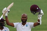 West Indies batter Kraigg Brathwaite raises his bat and helmet after scoring a century in a Test against Australia.