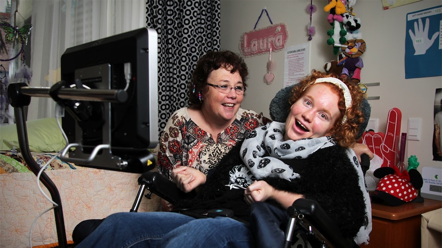 Laura Boyd smiles from her wheelchair while mother Cathy looks at her in her bedroom.