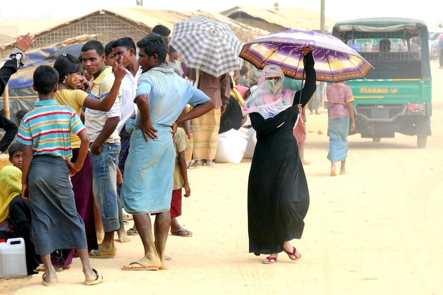 A woman holds a purple umbrella as she walks through the dusty refugee camp.