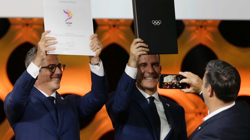 Casey Wasserman and Eric Garcetti hold up Olympic folders.