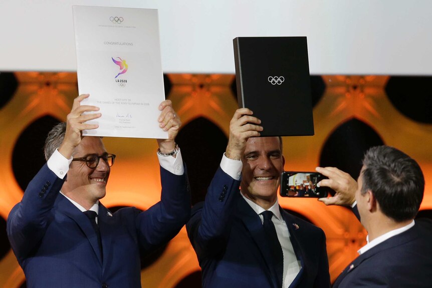 Casey Wasserman and Eric Garcetti hold up Olympic folders.