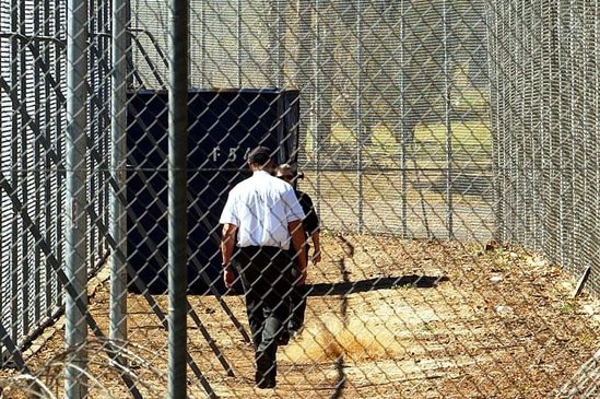 A guard walks between fences at an immigration detention centre