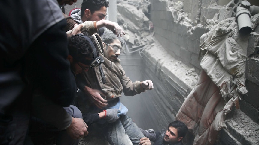 three men at the top of a trench surrounded by rubble pull another man from the rubble with the help of another below