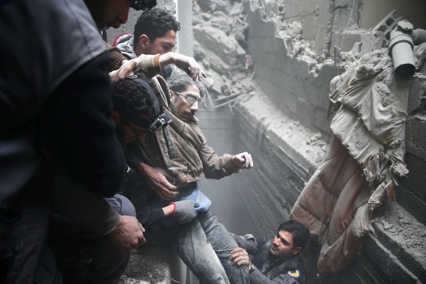 three men at the top of a trench surrounded by rubble pull another man from the rubble with the help of another below.