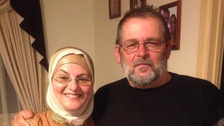 A man wearing glasses and a black jumper next to a smiling woman wearing gold clothing.