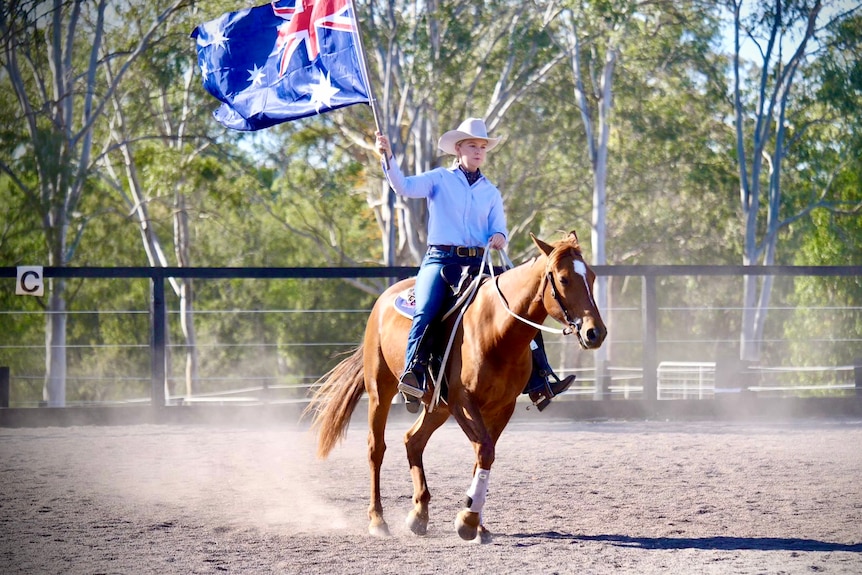 A woman carries an Australian flag while riding a horse.