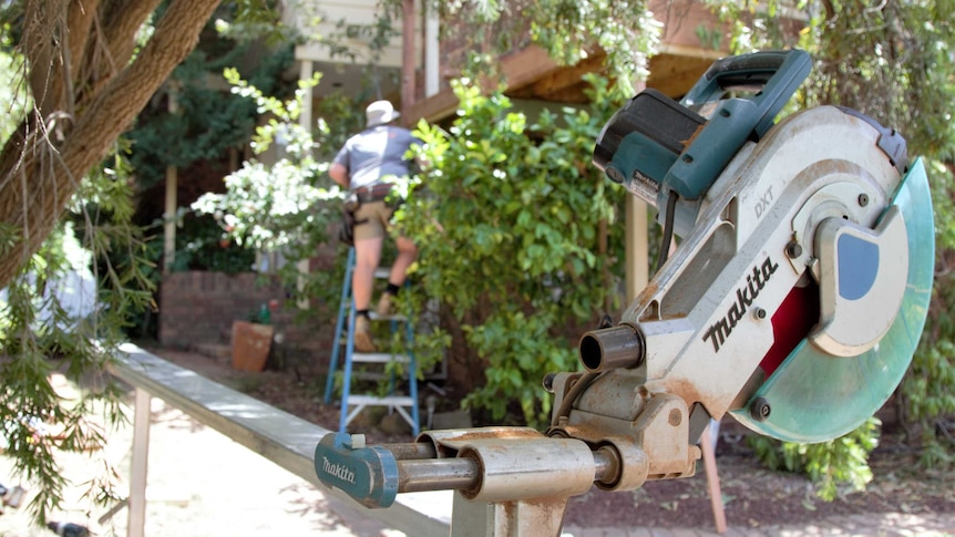 A tradesperson works on a house with a Makita circular saw in the foreground.