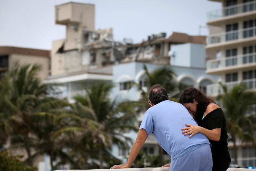 A couple stands near the partially collapsed building amid the search and rescue effort