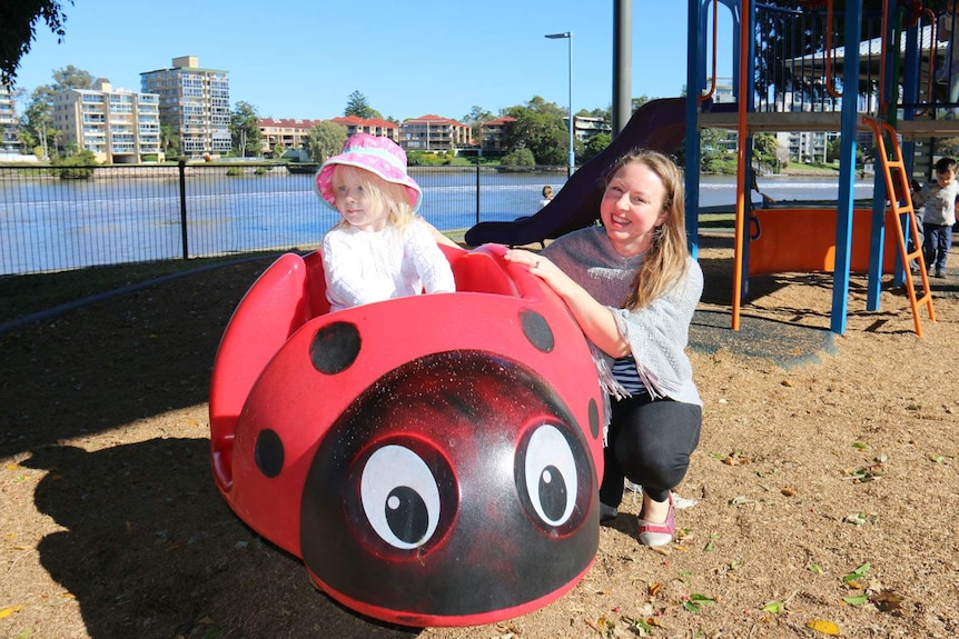Clarissa Brown in a Brisbane playground with her daughter Emmeline Brown sitting in ladybird shaped play equipment.