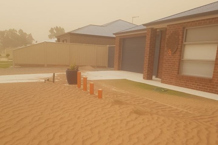 The lawn in front of a brick house on what looks like a suburban street is covered in thick sand.
