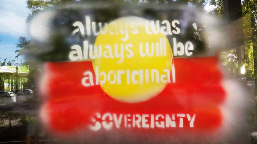 An Aboriginal flag, with writing 'always was, always will be Aboriginal sovereignty' on a window.