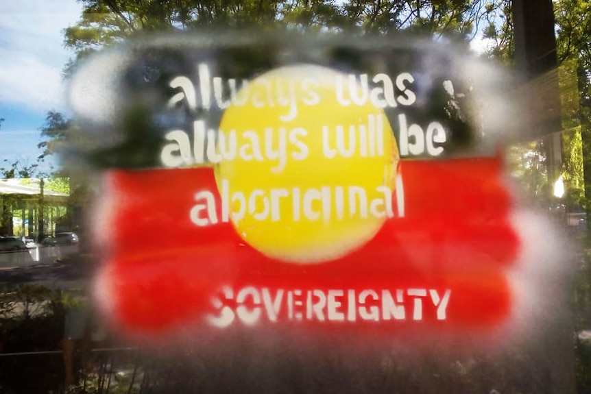 An Aboriginal flag, with writing 'always was, always will be Aboriginal sovereignty' on a window.
