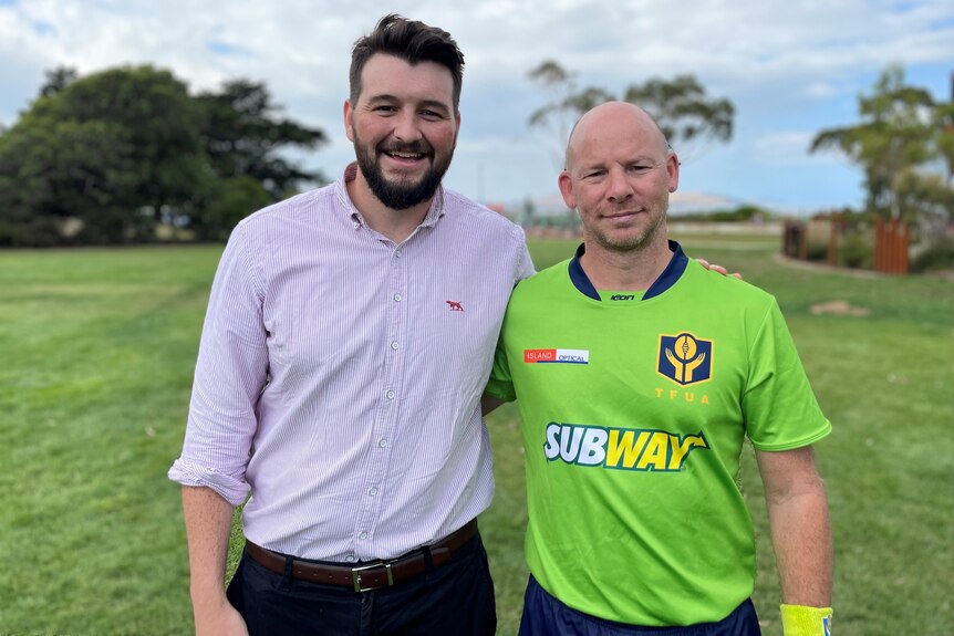 Two men stand on a sports ground, one wears an Aussie rules umpire's uniform