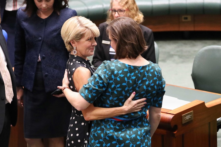 Julie Bishop, wearing a black polka dot top, puts an arm around Kelly O'Dwyer in the House of Representatives.