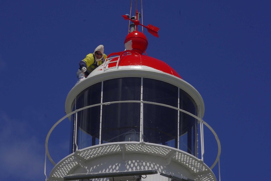 man on top of lighthouse painting it red