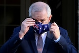 Prime Minister Scott Morrison adjusts his Australian flag mask at a media conference. 