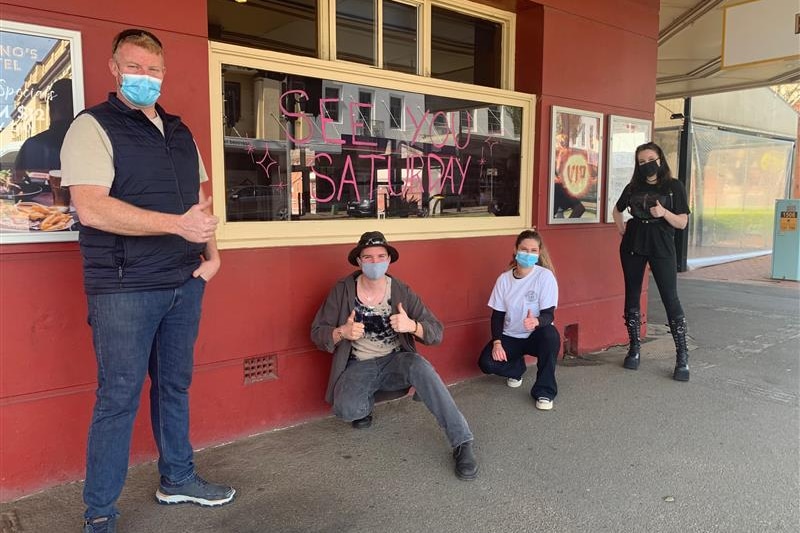 Four people in COVID masks sit and stand outside a pub looking happy