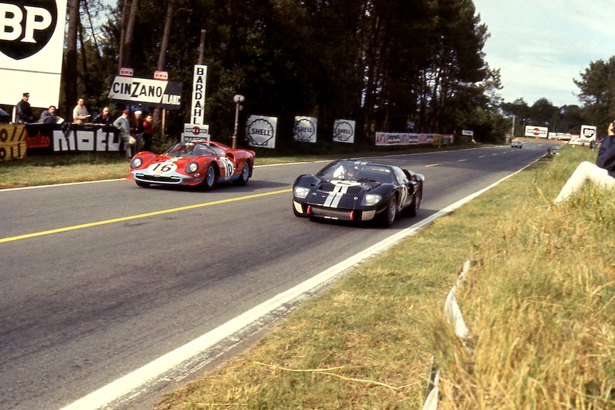 Two cars doewn the striaght, a red Ferrari and a black Ford, battle for the lead of the race.