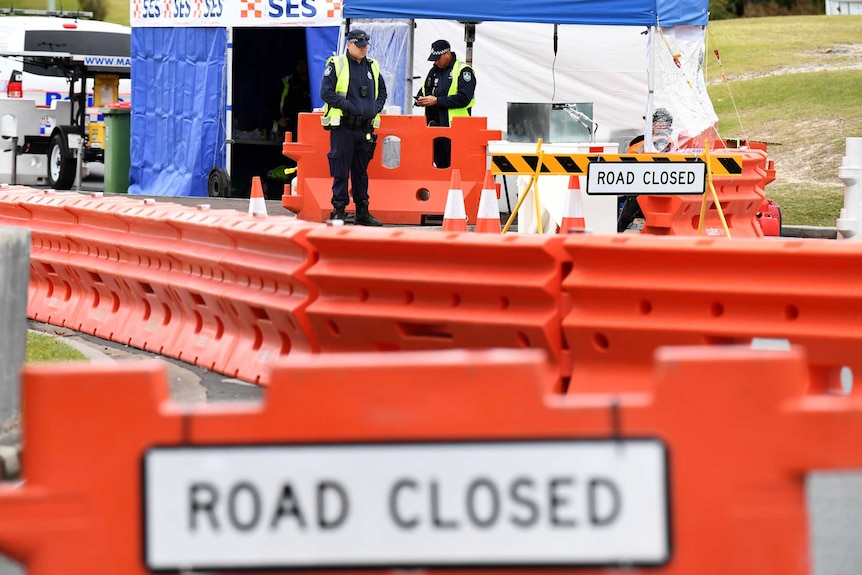 Police stand at a road block with barricades and road closed signs.