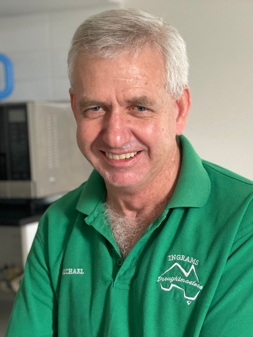 A man with grey hair smiles. He is wearing a green polo shirt.