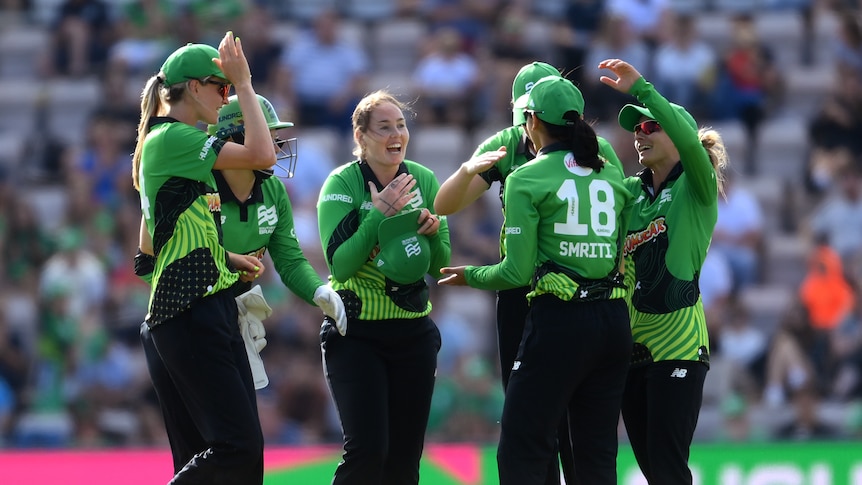 An excited cricket smiles as her teammates surround her to celebrate.