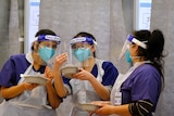 Three nurses in PPE inspect a needle.