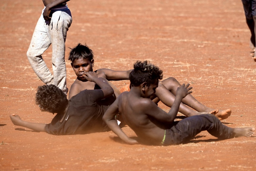 three kids lying on the ground after a contest while another walk past in the foreground