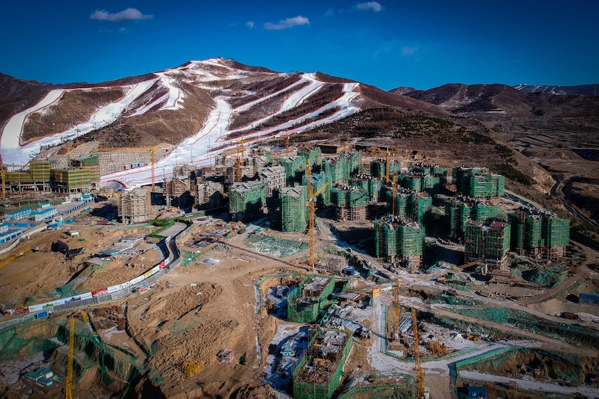 Construction and cranes on buildings sitting on mountains with skinny ski slopes.