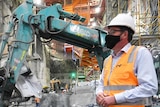 Daniel Andrews, dressed in a hard hat and high-vis, stands in front of heavy machinery on a construction site.