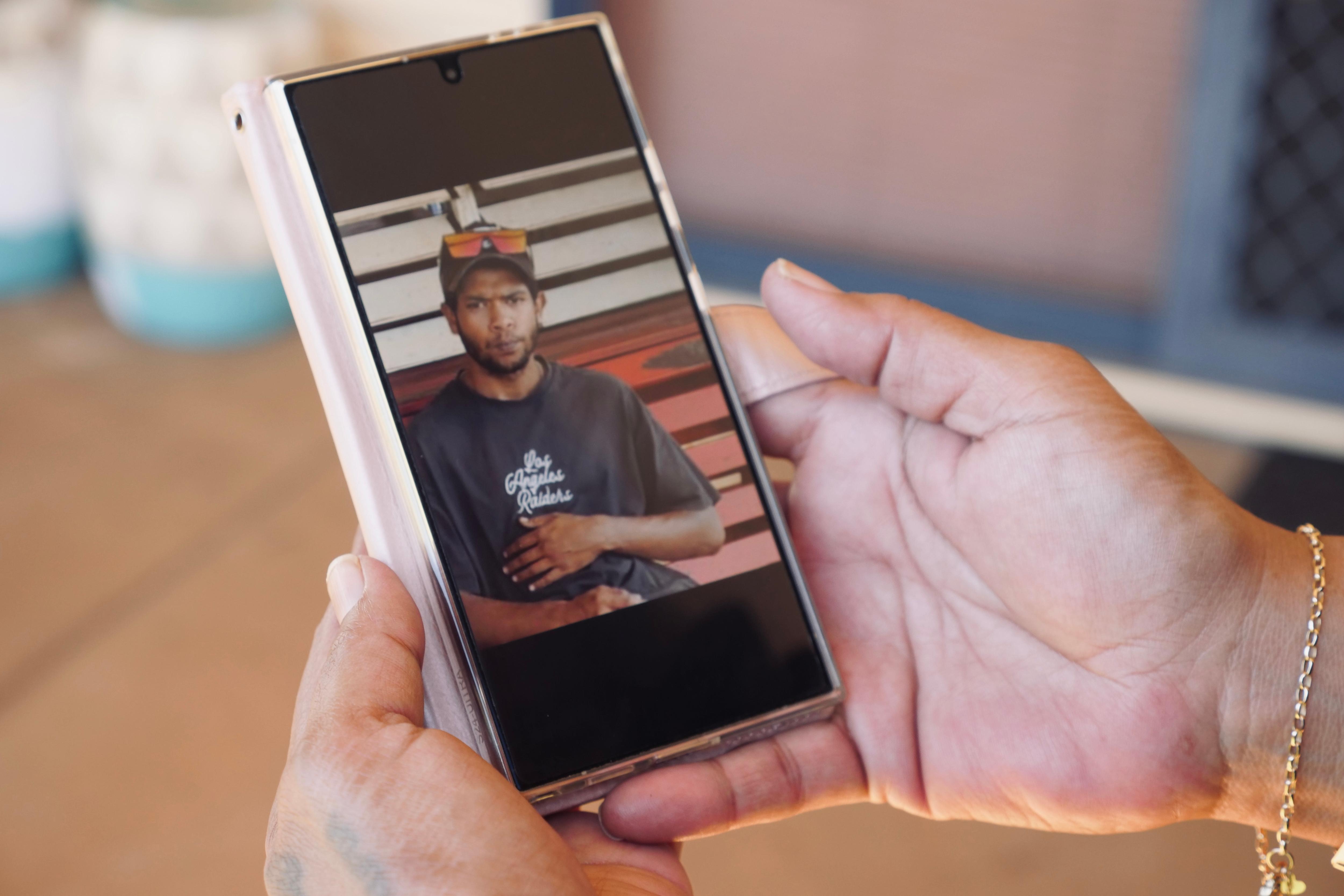 A woman's hands hold a phone displaying an image of a young man in a cap.