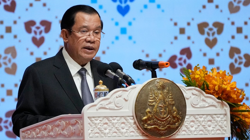 Man with glasses in black suit speaks from behind a podium.