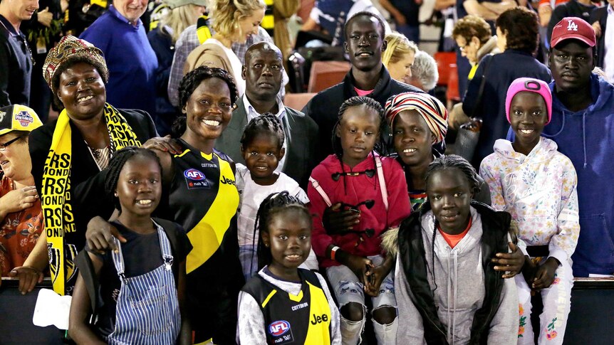 Akec Makur Chuot in an AFLW uniform posing in a group photo at a game with 10 family members