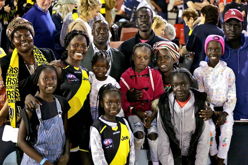 Akec Makur Chuot in an AFLW uniform posing in a group photo at a game with 10 family members
