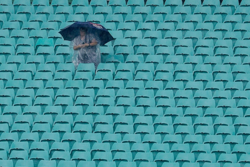 A fan in a rain poncho sits under an umbrella in the rain waiting for the T20 World Cup semi-final between England and India.
