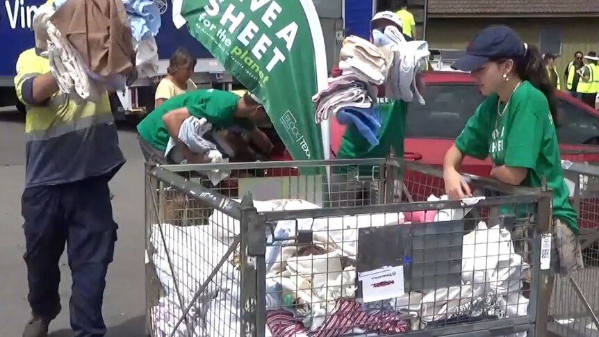 volunteers in green t-shirts and hi-vis load sheets and towels into a recycling container