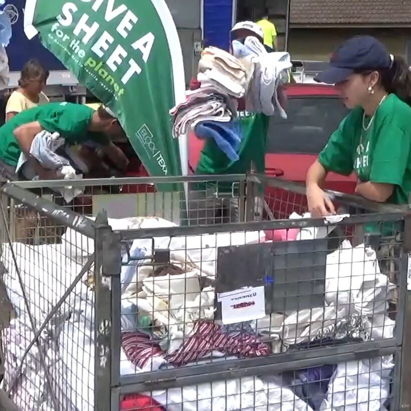 volunteers in green t-shirts and hi-vis load sheets and towels into a recycling container