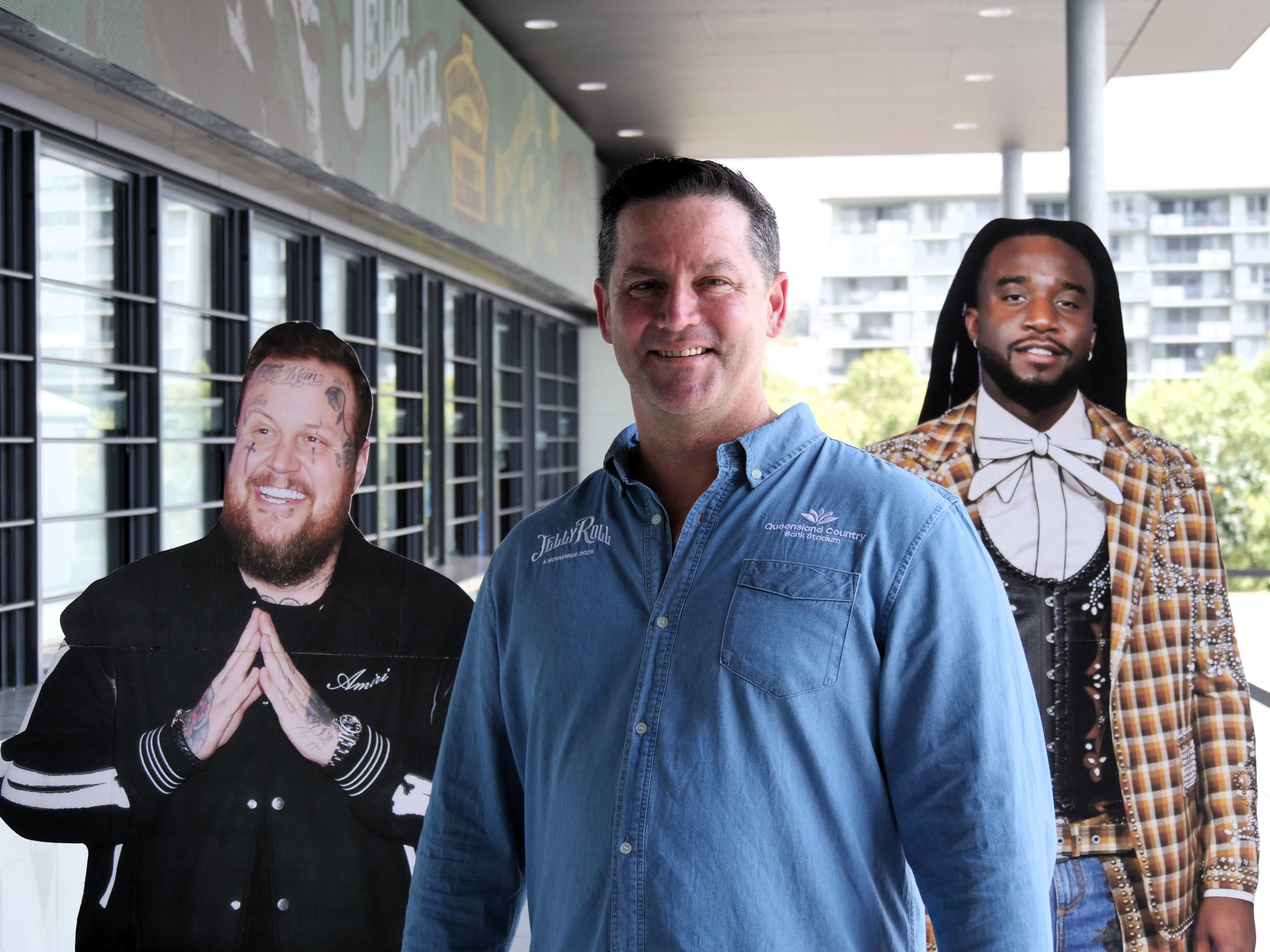 A man wearing a blue button down beside two cardboard cut outs.