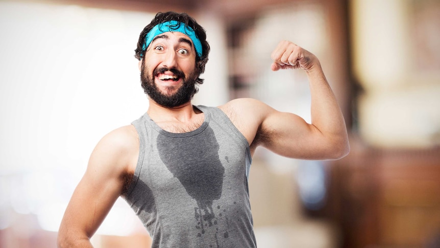 A man with a beard wearing a blue sweatband and grey singlet with a sweat stain on the front