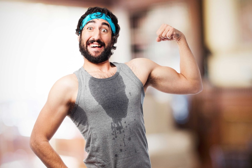 A man with a beard wearing a blue sweatband and grey singlet with a sweat stain on the front