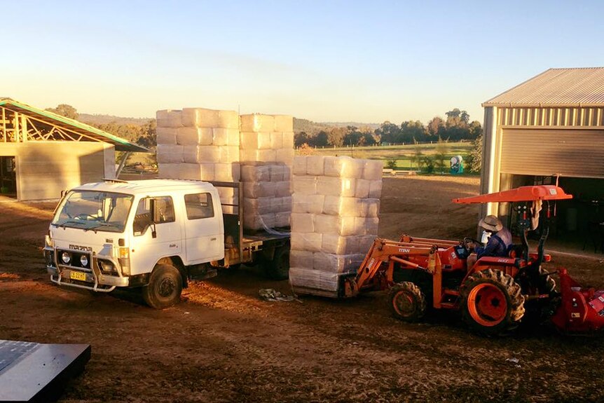 A tractor with a forklift attachment getting bales of a building product wrapped in plastic off a truck