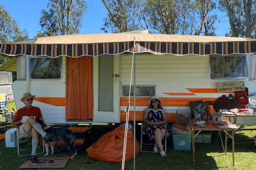 vintage caravan with two people and a dog relaxing outside it