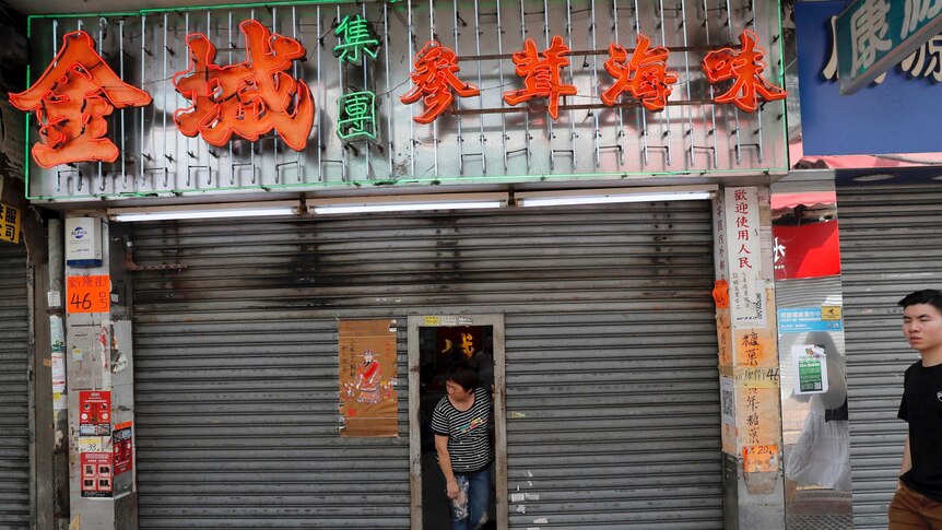 A Chinese shop owner looks out from her shuttered store as protesters march in Hong Kong.