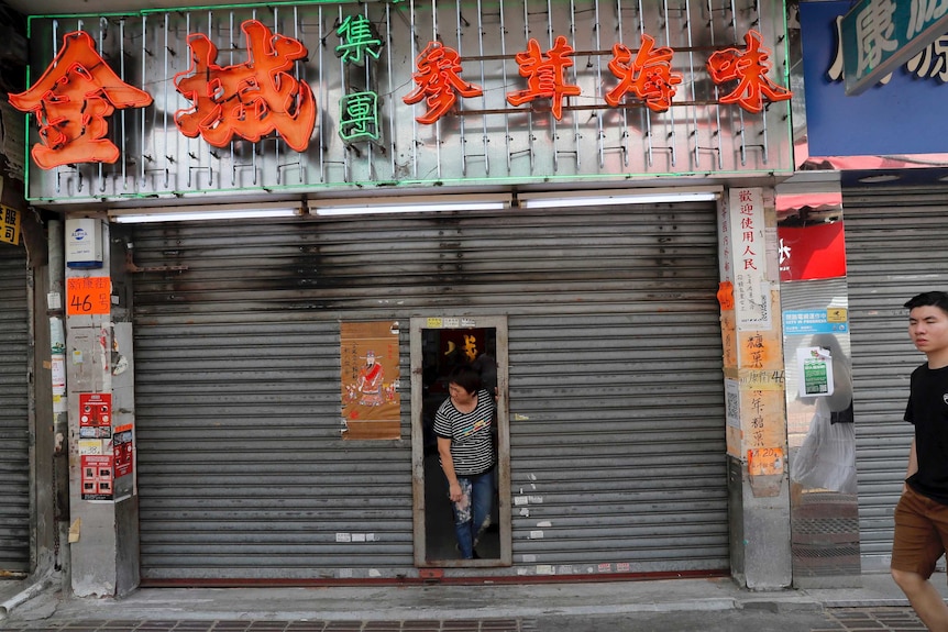 A Chinese shop owner looks out from her shuttered store as protesters march in Hong Kong.