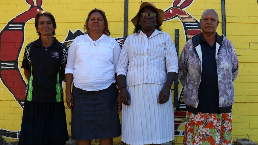 Anne-Marie Lee, Helen Lee, Anita Painter, Ruth Kelly stand next to a bright yellow wall, painted with kangaroos